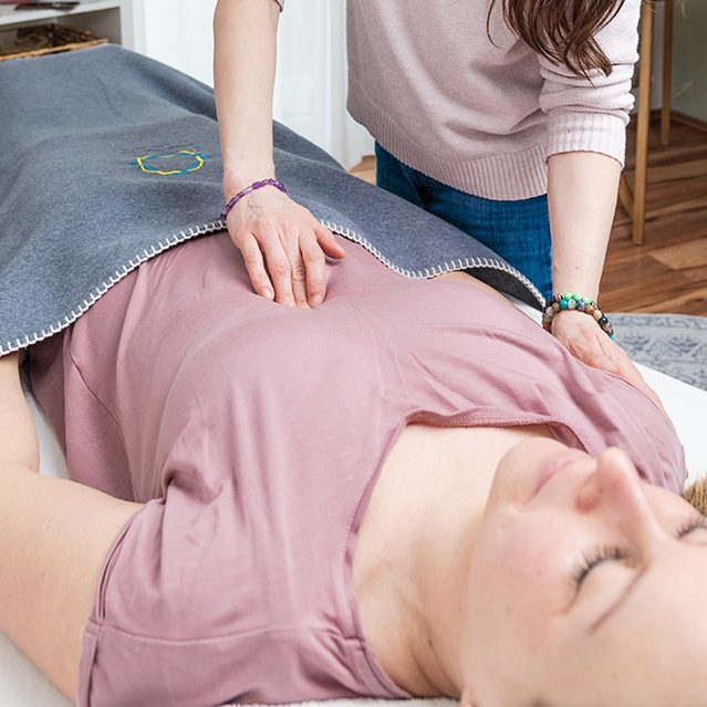 Eine Frau liegt entspannt auf einer Liege, während Beate Kammerbauer eine Behandlung am Bauch durchführt.