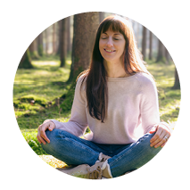 Beate Kammerbauer mit geschlossenen Augen, im Schneidersitz auf dem Waldboden.